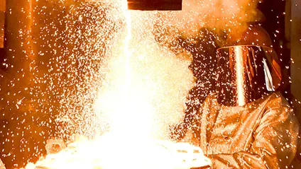 Factory worker wearing protective clothing creating liquid metal. Image is orange with heat and sparks