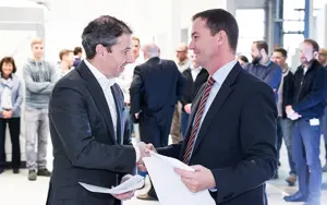 Two men in suits shaking hands and holding paperwork